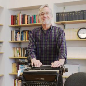 Professor Jack Lule stands behind a typewriter in the meeting room of Coppee Hall on Nov. 18.