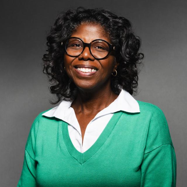  Robin Sundaramoorthy wearing a green sweater and a white collared shirt smiling for her headshot with a black backdrop.